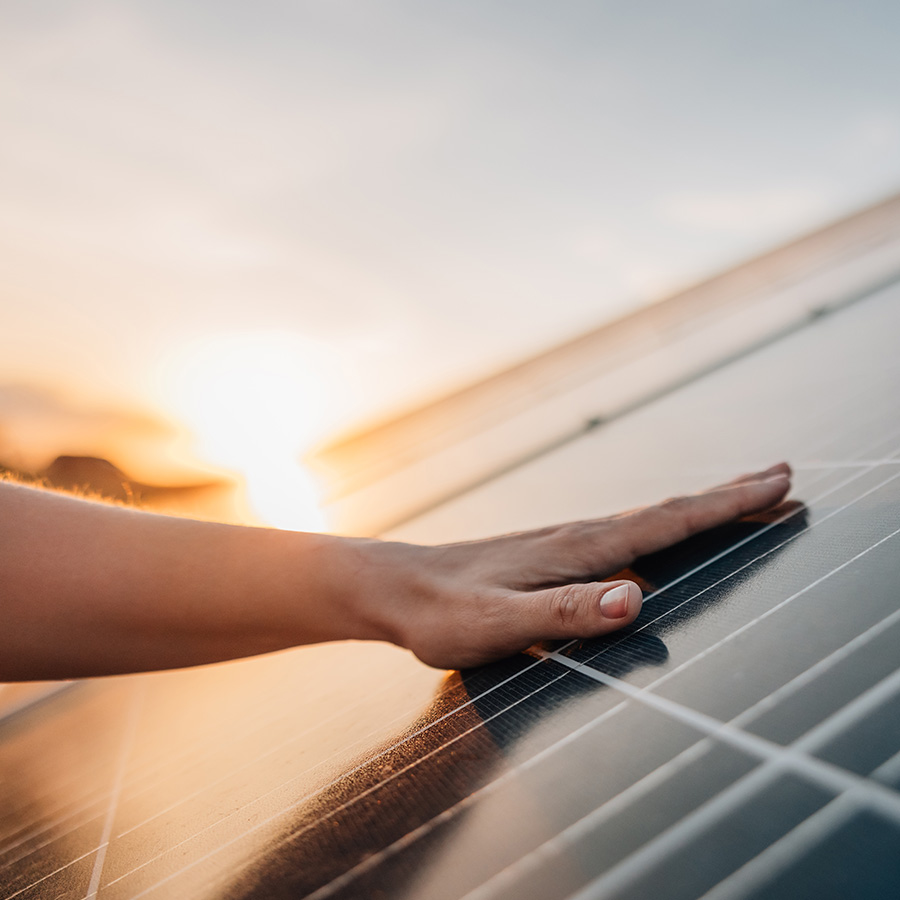 Eine Hand liegt bei Sonnenutergang auf der Fläche eines Solarpanels einer großen Erzeugeranlage.