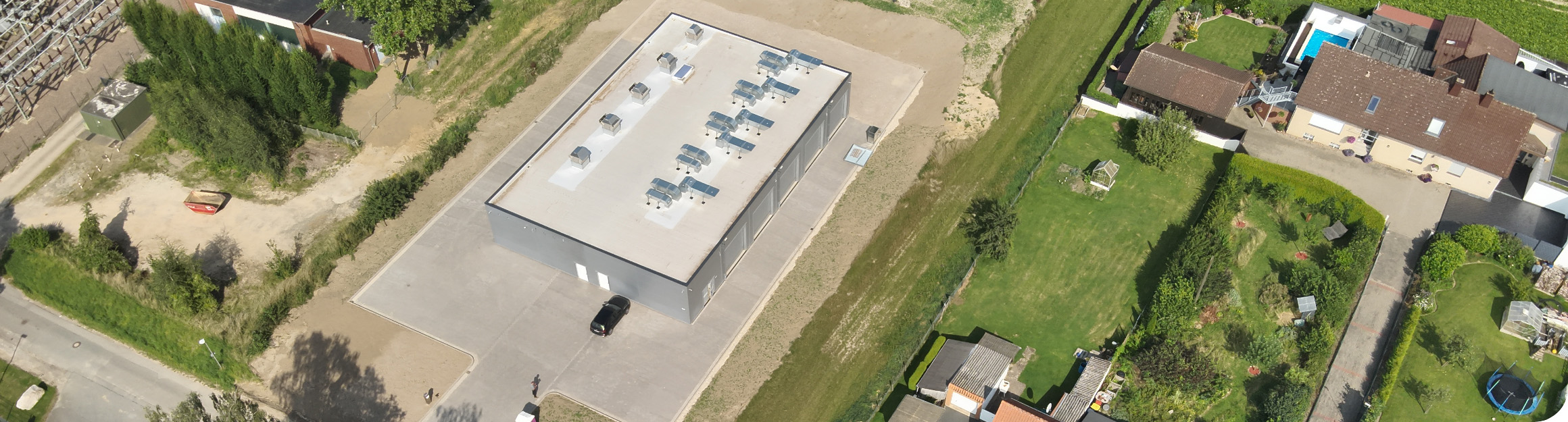 Blick von oben aus der Luft auf eine Halle, in der sich eine Batteriespeicheranlage befindet, innerhalb eines Wohngebiets.