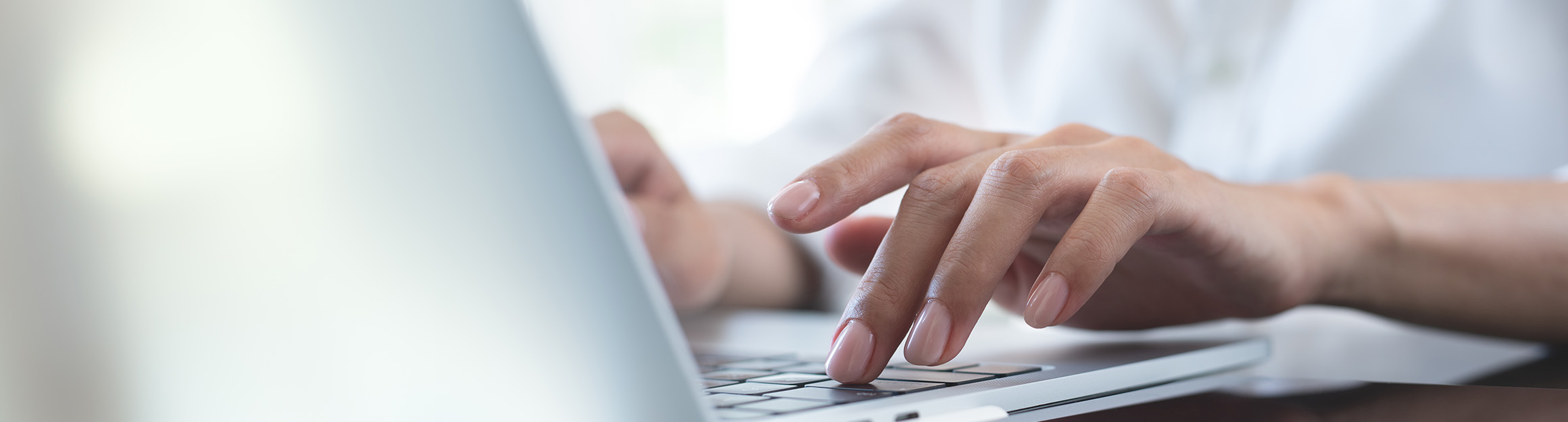Hände einer Person, die konzentriert auf einer Laptop-Tastatur tippt, mit weichem Lichteinfall und unscharfem Hintergrund.
